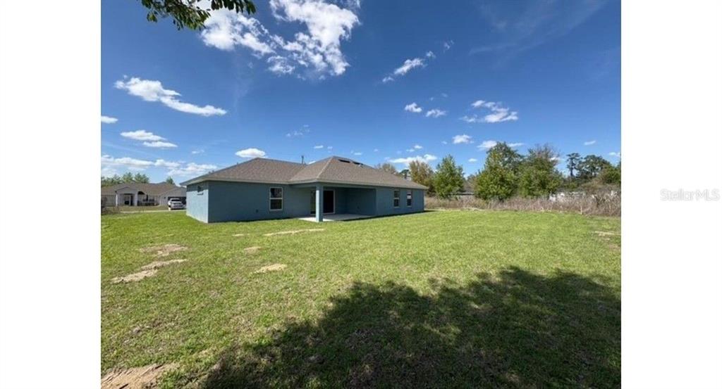 A blue single-story house with a covered back patio sits on a large grassy lot — 12833 SW 72ND TERRACE ROAD, OCALA, FL