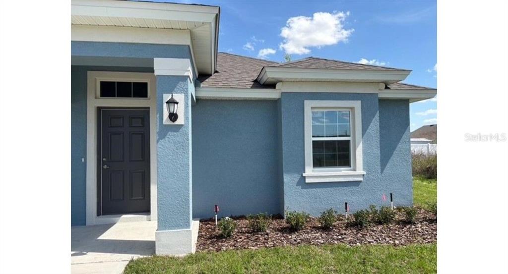 A blue stucco house exterior features a dark front door, a window, and landscaping — 12833 SW 72ND TERRACE ROAD, OCALA, FL