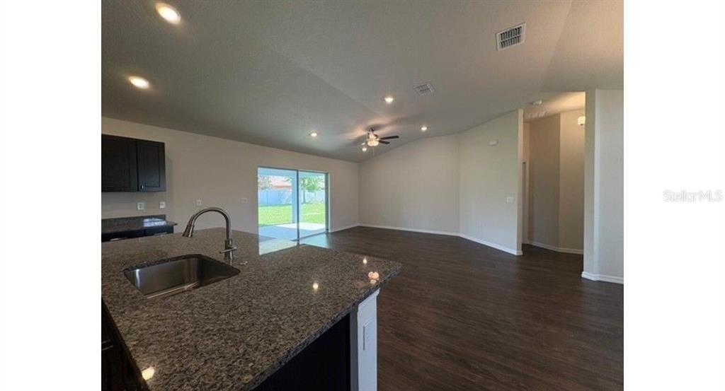 A kitchen island with a granite countertop overlooks an open-concept living area with dark flooring — 12833 SW 72ND TERRACE ROAD, OCALA, FL