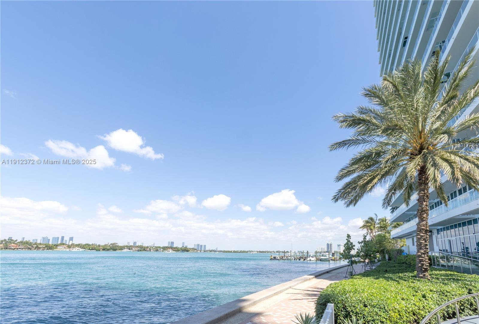 A paved walkway runs along the waterfront next to a modern high-rise building and palm — 520 West Ave # 1102, Miami Beach FL 33139, MIAMI BEACH, FL