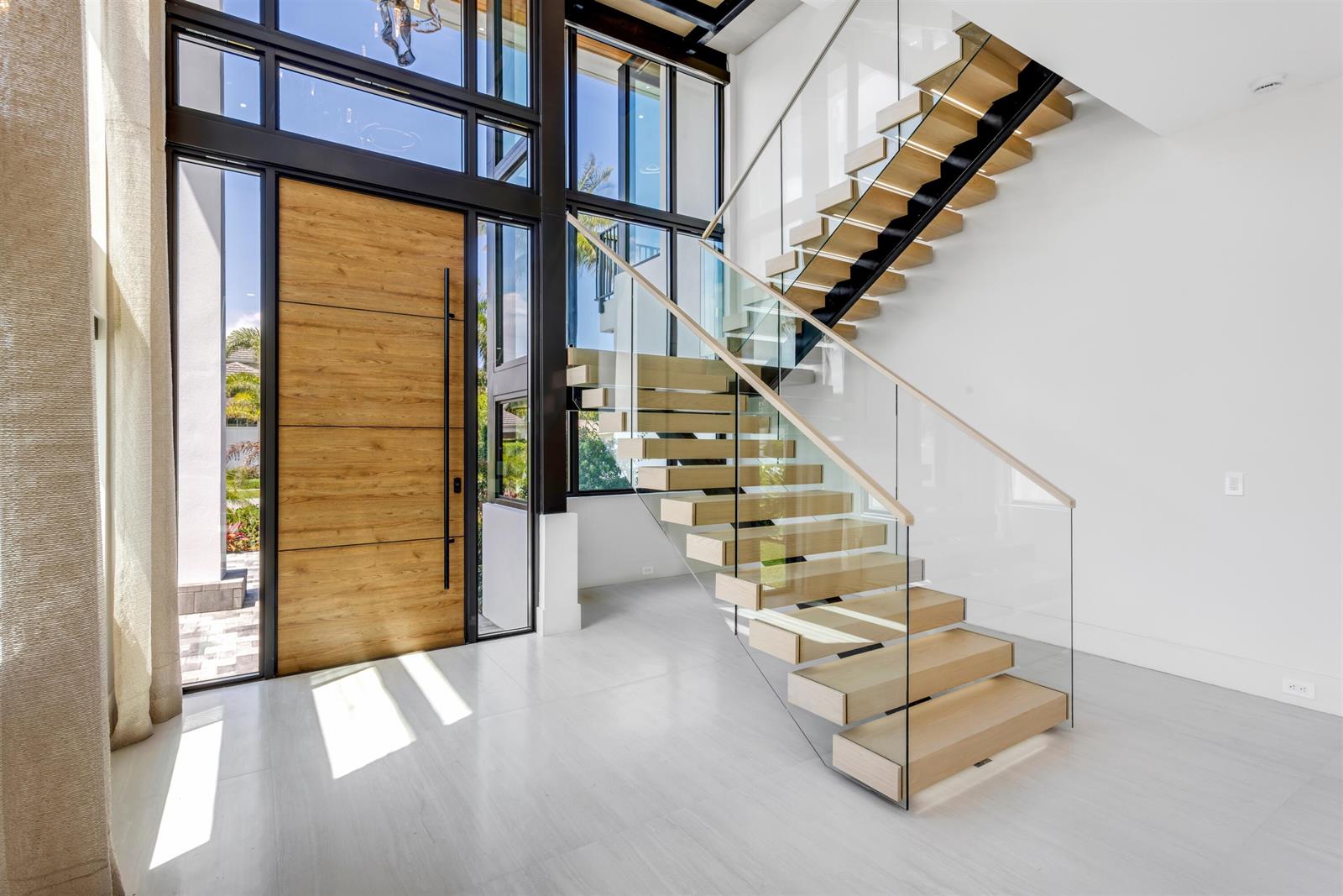 A modern entryway features a large wood door, floor-to-ceiling windows, and a floating glass staircase — 310 NE 2nd Street, Boca Raton FL 33432, BOCA RATON, FL