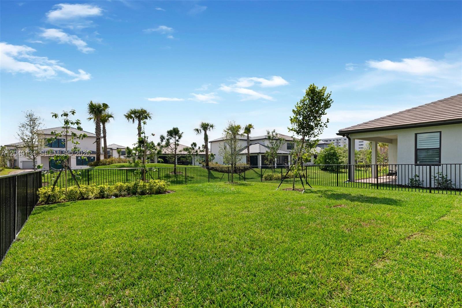 A grassy backyard features a black metal fence, young trees, and neighboring suburban houses — 4470 Waterside Dr, Oakland Park FL 33309, OAKLAND PARK, FL