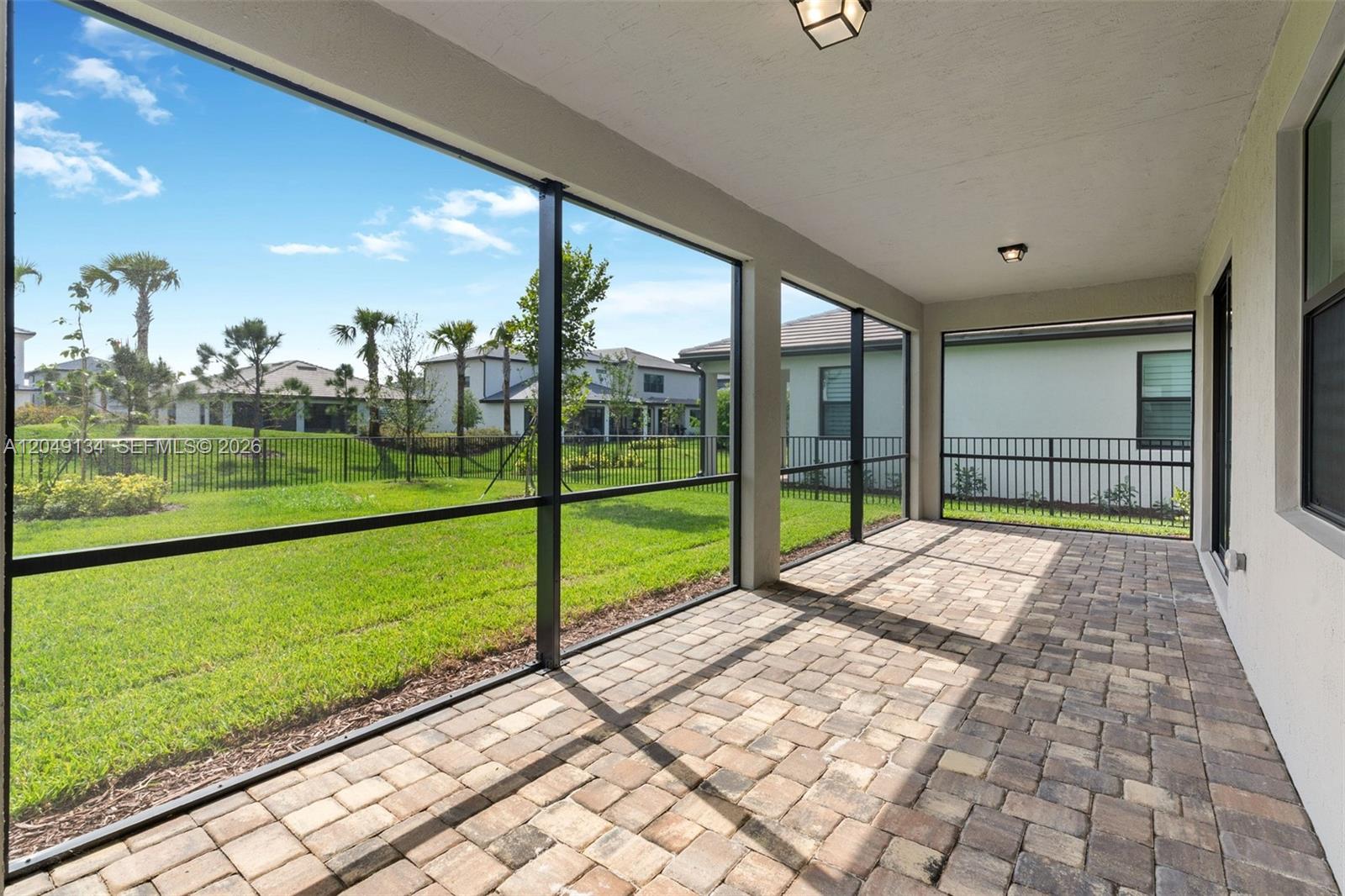 A screened-in patio features paver flooring and views of a grassy backyard and neighboring houses — 4470 Waterside Dr, Oakland Park FL 33309, OAKLAND PARK, FL
