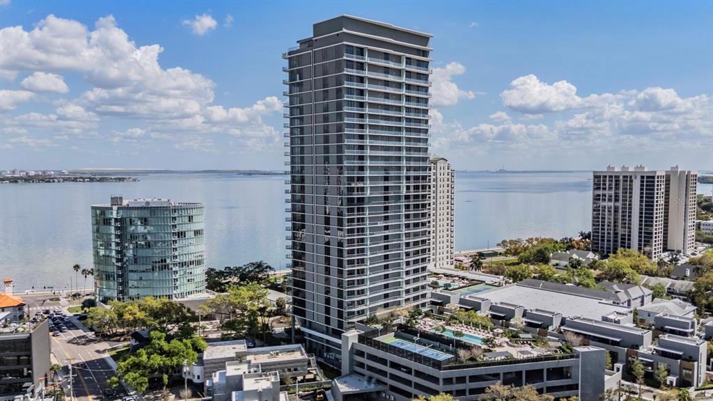 An aerial view shows a tall modern residential tower beside a bay and smaller buildings — 3015 S YSABELLA AVENUE UNIT 2003, TAMPA, FL