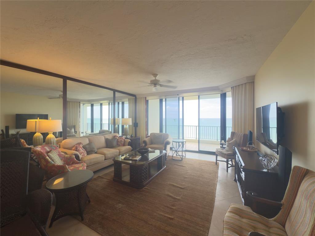 A living room features a large mirror wall, a beige sofa, and a balcony overlooking water — 800 Ocean Drive # 404, Juno Beach FL 33408, JUNO BEACH, FL