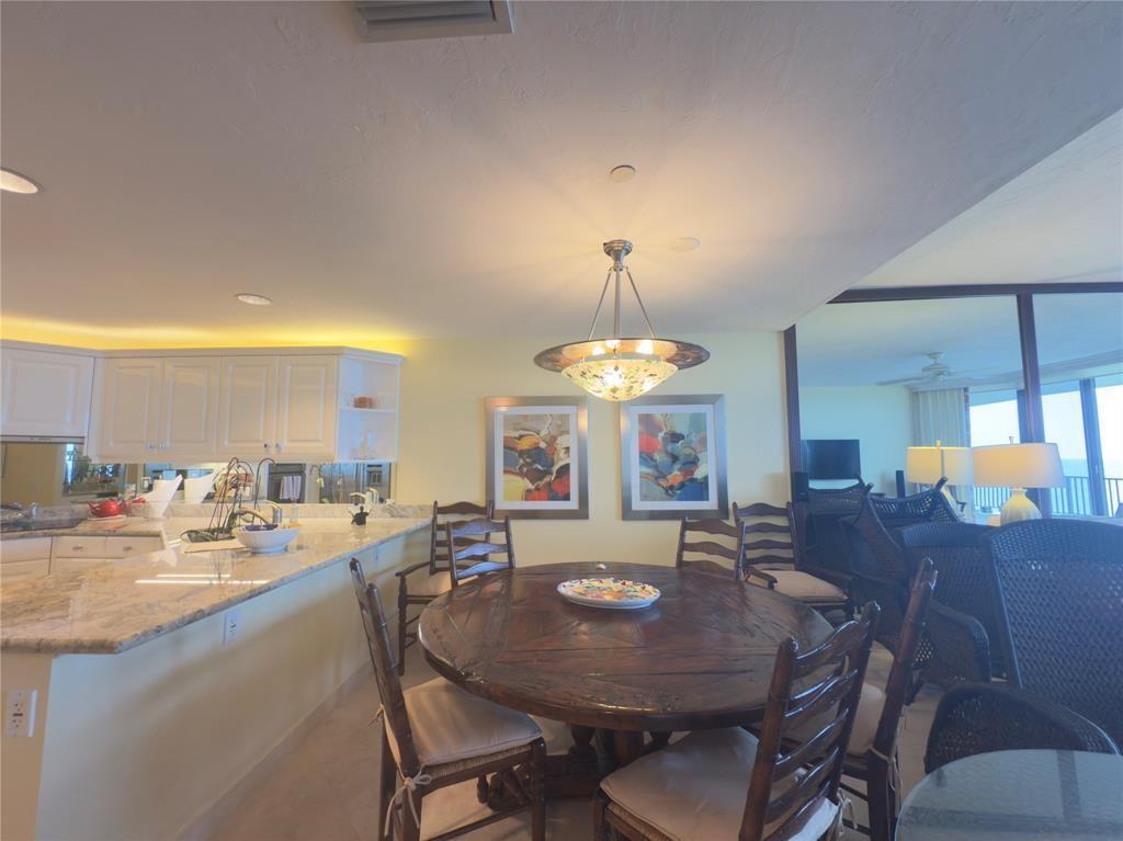 A dining area with a round wooden table, chairs, and a pendant light near a kitchen — 800 Ocean Drive # 404, Juno Beach FL 33408, JUNO BEACH, FL
