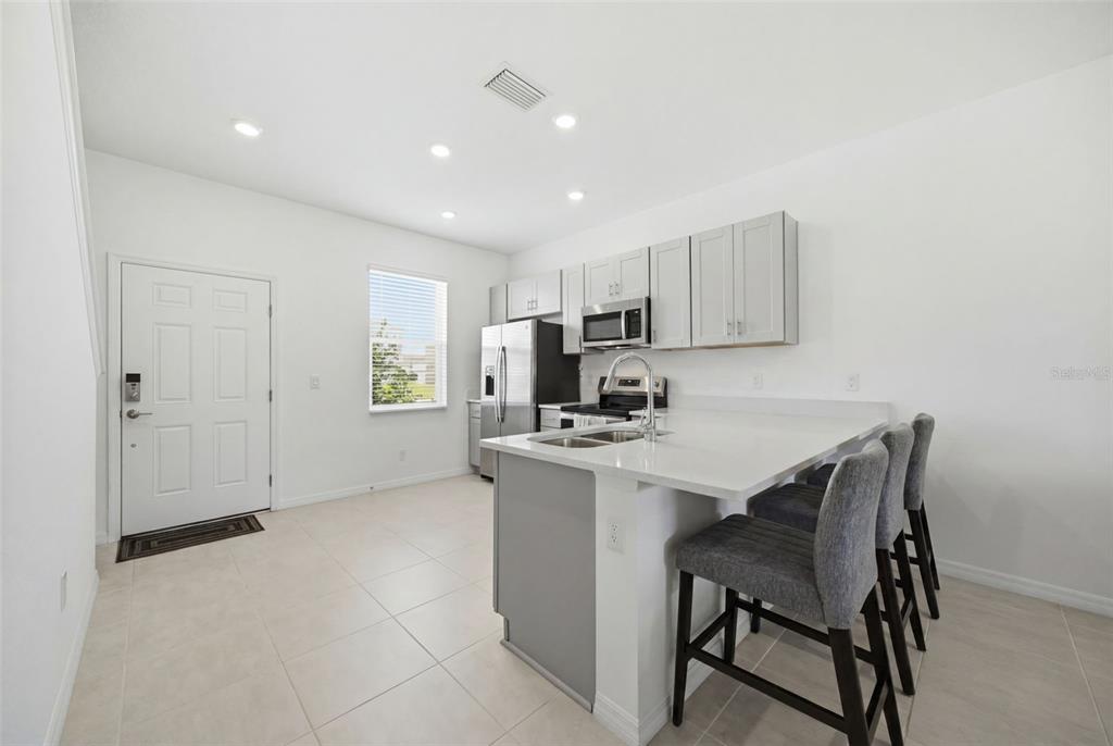 A kitchen features light gray cabinets, stainless steel appliances, a quartz island, and tile flooring — 16570 SAN NICOLA PLACE, BRADENTON, FL