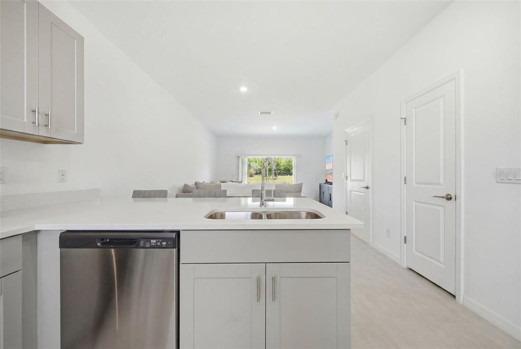 A kitchen island with a stainless steel dishwasher and sink faces a bright living area — 16570 SAN NICOLA PLACE, BRADENTON, FL