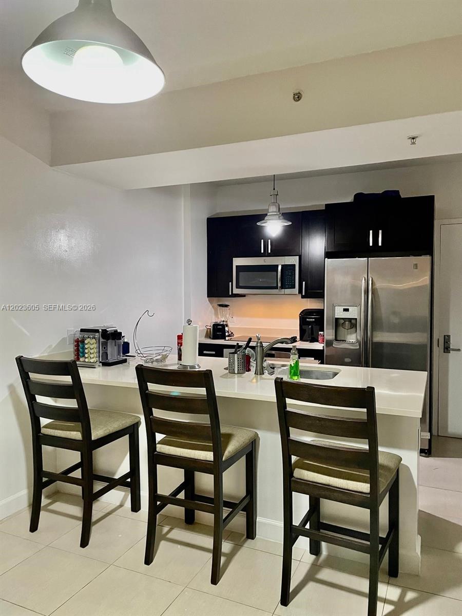 A kitchen features dark cabinets, stainless steel appliances, and a breakfast bar with three chairs — 333 NE 24th St # 1108, Miami FL 33137, MIAMI, FL