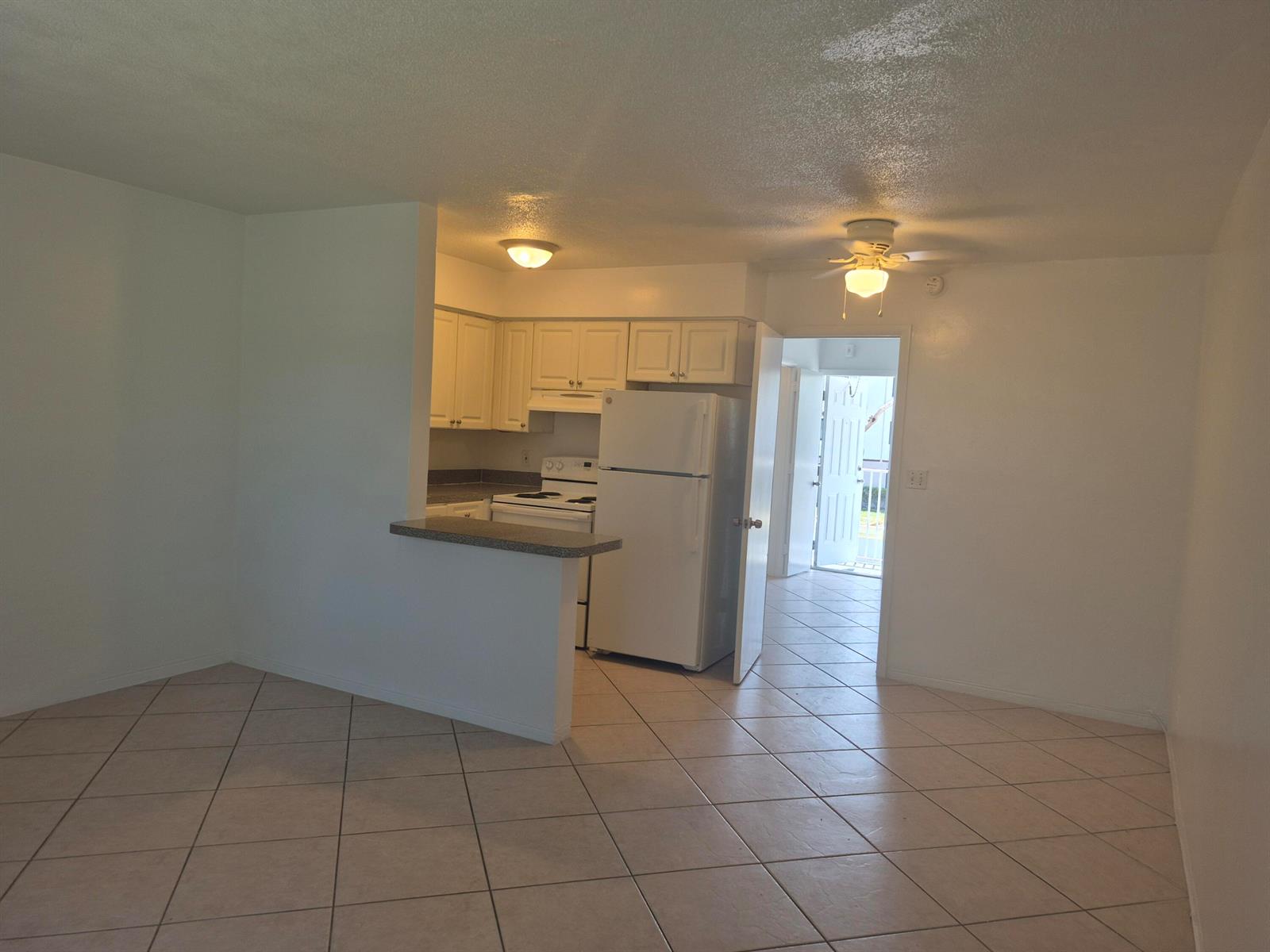 An open-concept kitchen with white cabinets and a breakfast bar overlooks a tiled living area — 1960 NE 48 Street # 9, Pompano Beach FL 33064, POMPANO BEACH, FL