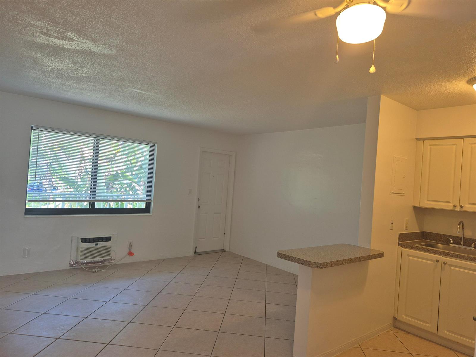 An open-concept living area with tile flooring, a window, an air conditioner, and a kitchen — 1960 NE 48 Street # 9, Pompano Beach FL 33064, POMPANO BEACH, FL