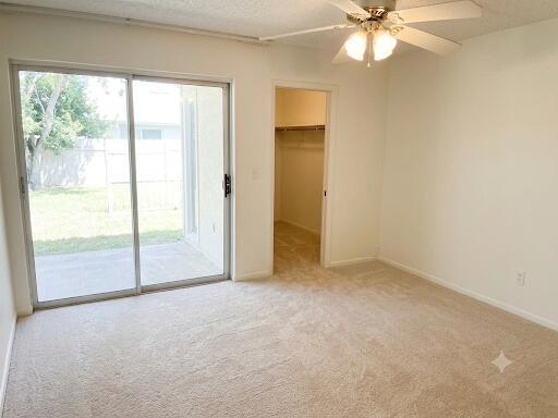A bedroom with beige carpet, a ceiling fan, a walk-in closet, and a sliding glass door — 1015 Ainslie A Drive, Boca Raton FL 33434, BOCA RATON, FL