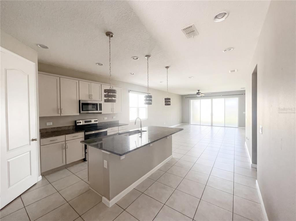 A kitchen with light cabinets, dark countertops, and an island opens to a living area — 2526 W END DRIVE, ST CLOUD, FL