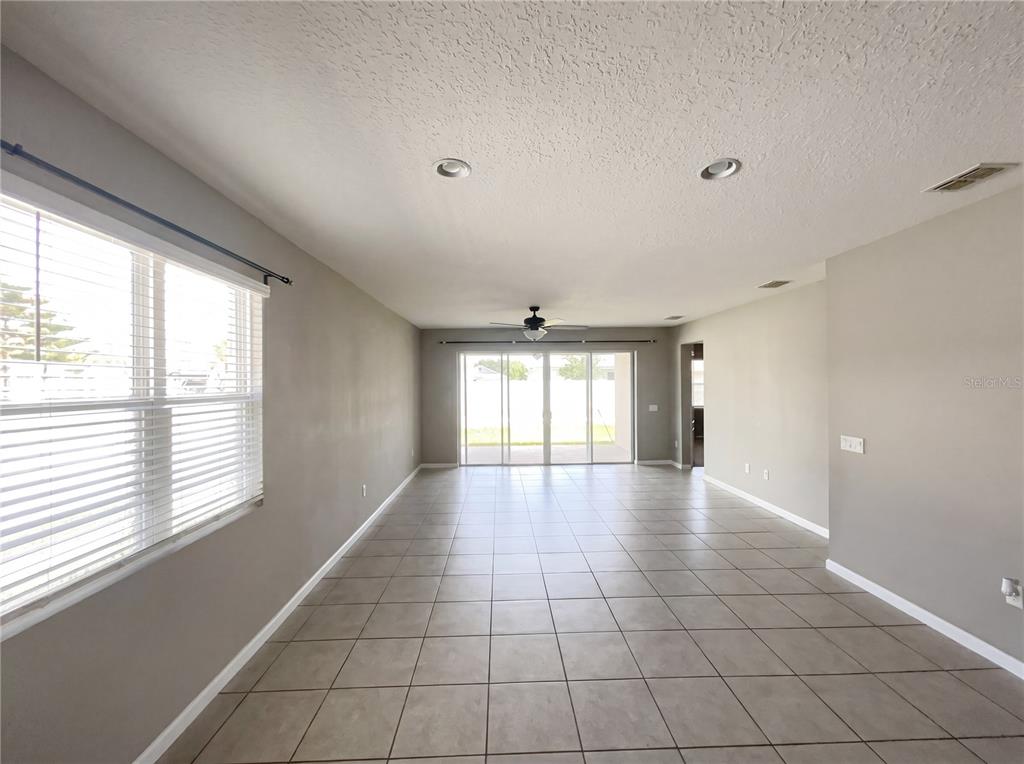 An empty living room features light gray walls, tile flooring, recessed lighting, and sliding glass doors — 2526 W END DRIVE, ST CLOUD, FL