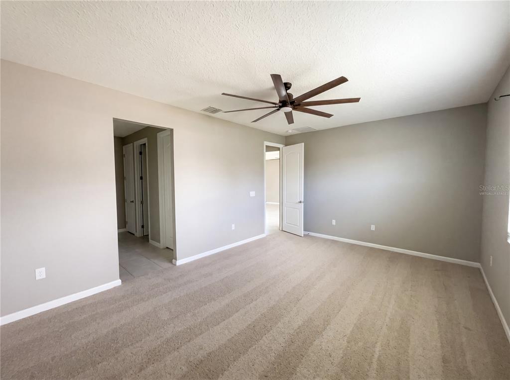 An empty bedroom features beige carpet, light gray walls, a ceiling fan, and two doorways — 2526 W END DRIVE, ST CLOUD, FL