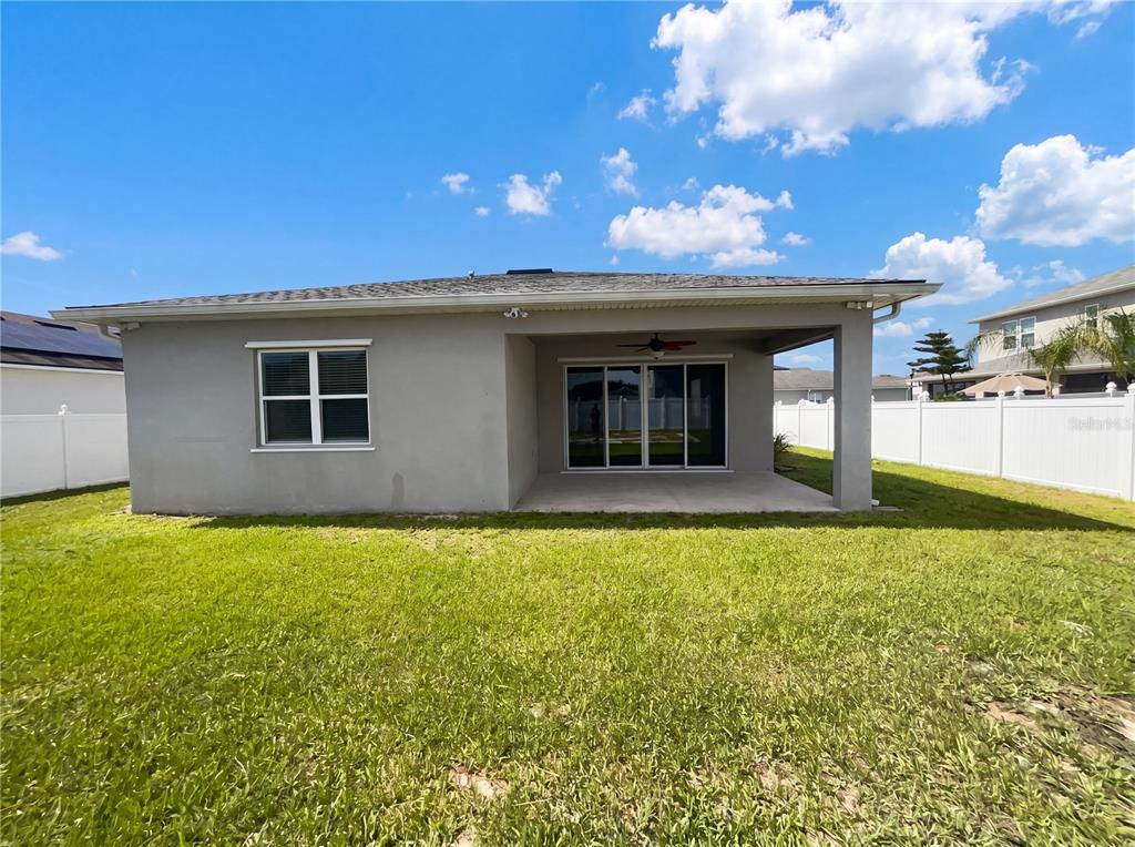 The rear exterior of a gray stucco house features a covered patio and sliding doors — 2526 W END DRIVE, ST CLOUD, FL