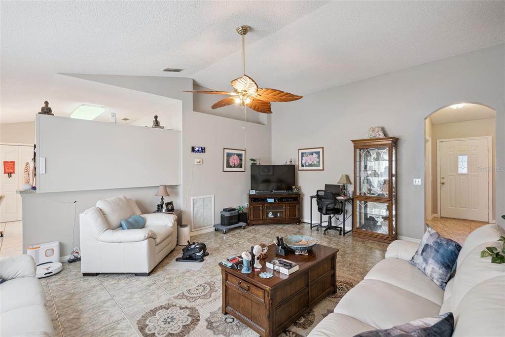 A living room features tile flooring, a vaulted ceiling with a fan, and white furniture — 2563 SHEFFIELD DRIVE, DELTONA, FL