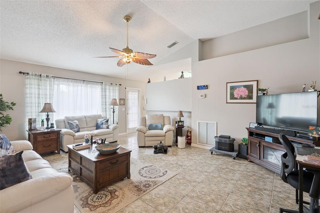 A living room features tile flooring, a vaulted ceiling with a fan, and white furniture — 2563 SHEFFIELD DRIVE, DELTONA, FL