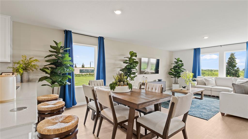 This open-concept living and dining area features light wood floors, blue curtains, and modern furniture — 696 RUTH AVENUE, HAINES CITY, FL
