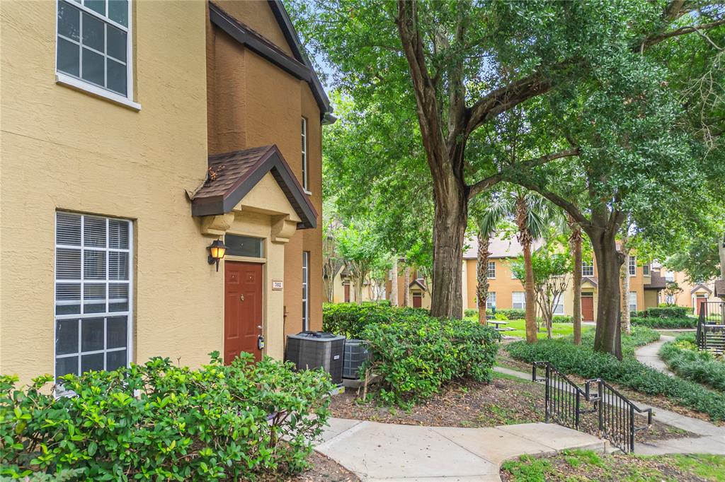 The exterior of a multi-story tan apartment building with a red front door and landscaping — 6324 RALEIGH STREET UNIT 702, ORLANDO, FL