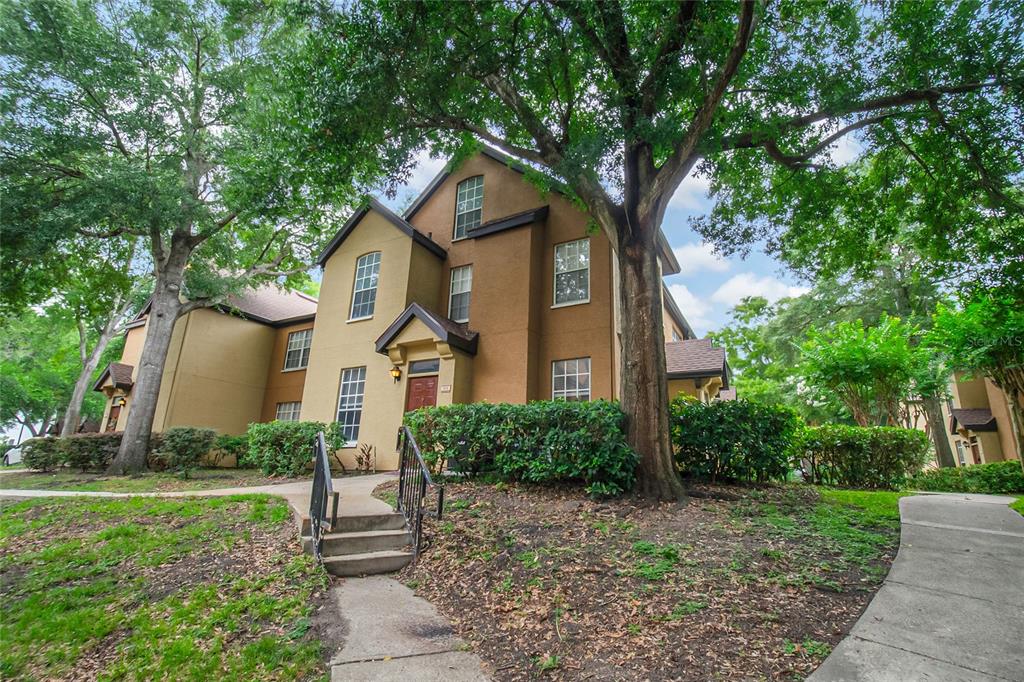 A three-story tan stucco apartment building with a brown roof and surrounding trees and landscaping — 6324 RALEIGH STREET UNIT 702, ORLANDO, FL