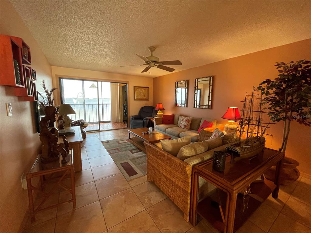 A living room features tile floors, a wicker sofa, a model ship, and a balcony view — 14459 RIVER BEACH DRIVE UNIT C122, PORT CHARLOTTE, FL