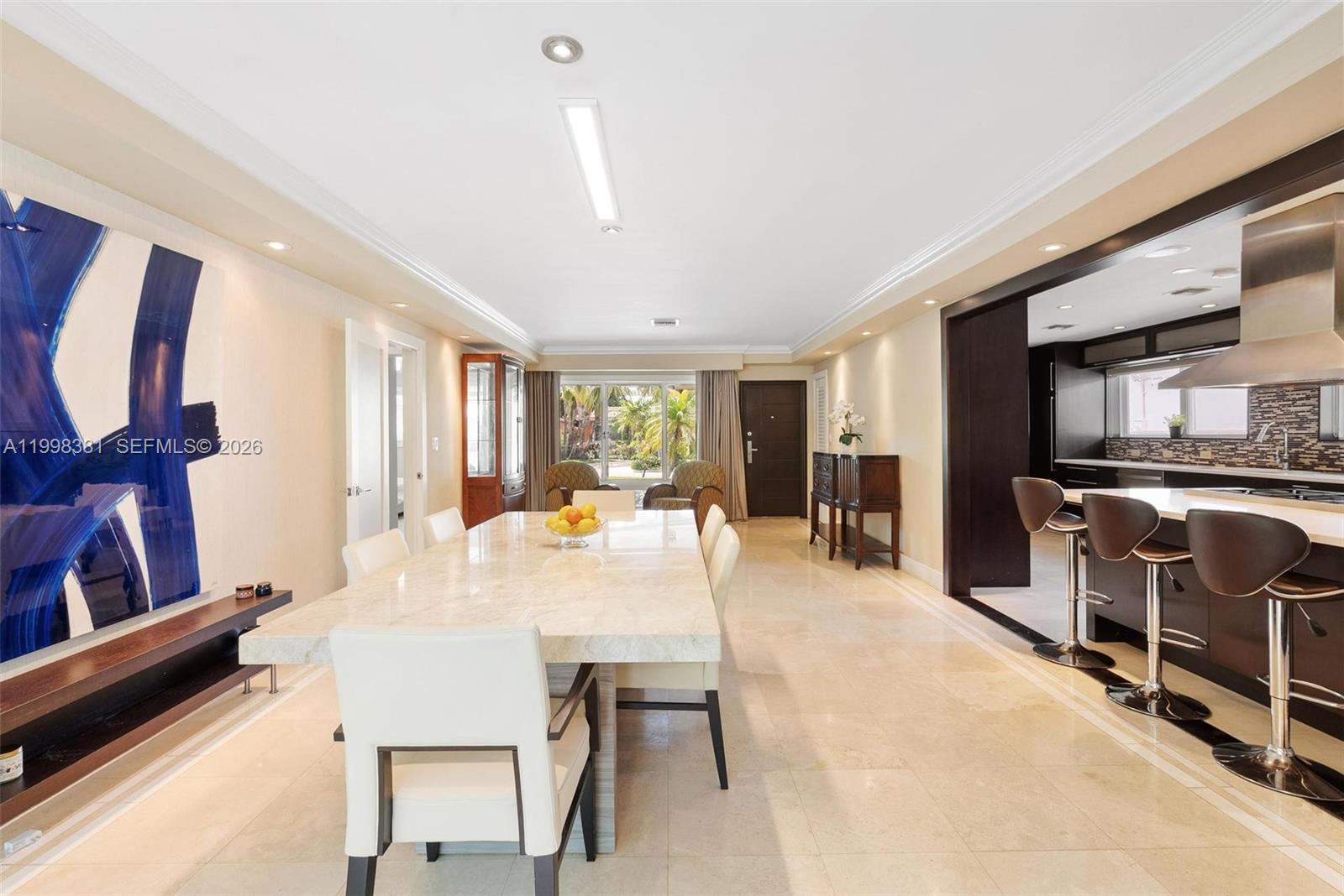 A dining area with a stone table sits adjacent to an open-concept kitchen with bar seating — 9141 Abbott Ave, Surfside FL 33154, SURFSIDE, FL