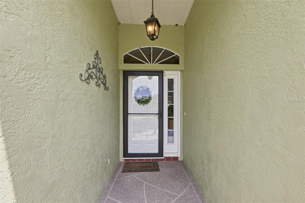 A covered entryway features light green stucco walls, a glass storm door, and a hanging lantern — 2242 W DEL WEBB BOULEVARD, SUN CITY CENTER, FL