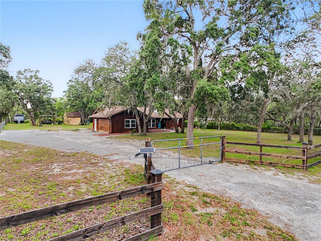 A gravel driveway leads to a brown house behind a metal gate and wooden fence — 5253 W ROCHELLE STREET, HOMOSASSA, FL