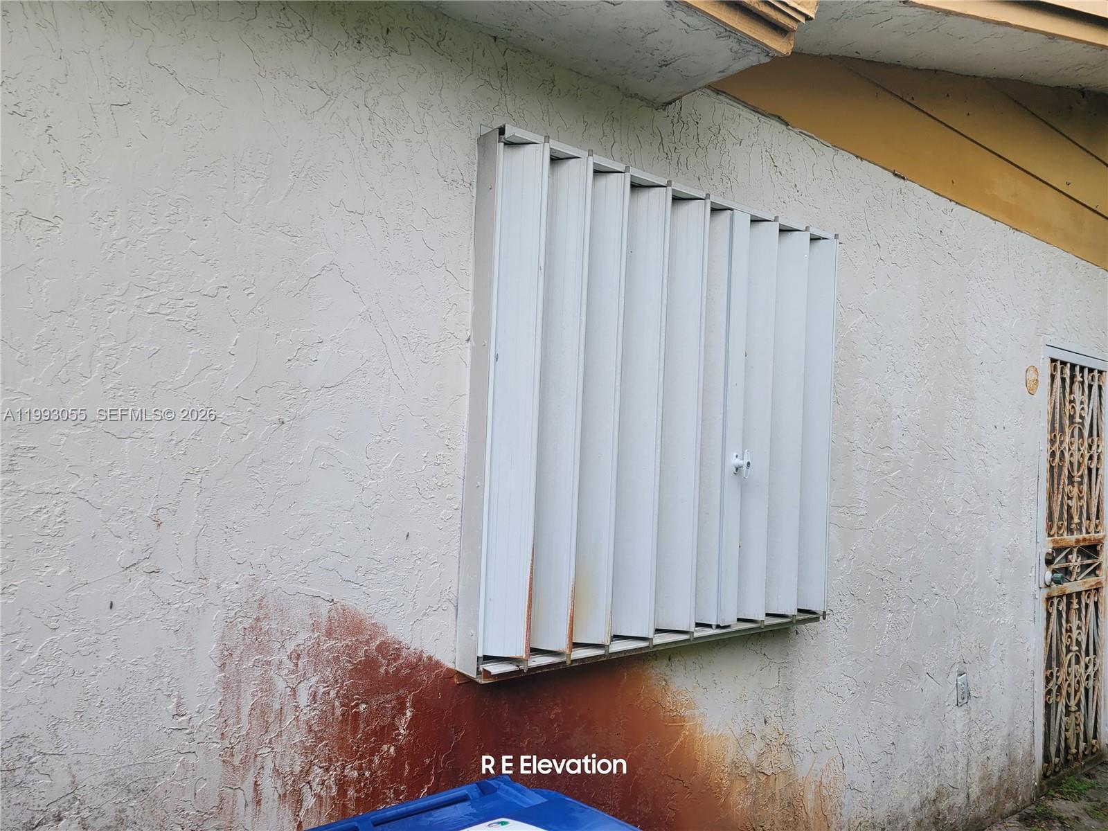An exterior view of a stucco wall featuring vertical accordion hurricane shutters and a metal door — 1149 NW 45th Ave, Lauderhill FL 33313, LAUDERHILL, FL