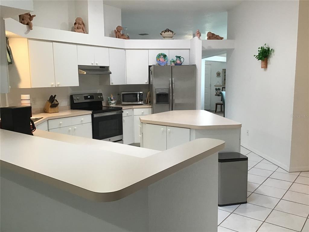 A kitchen features white cabinets, stainless steel appliances, a central island, and tiled flooring — 2984 TUSKET AVENUE, NORTH PORT, FL