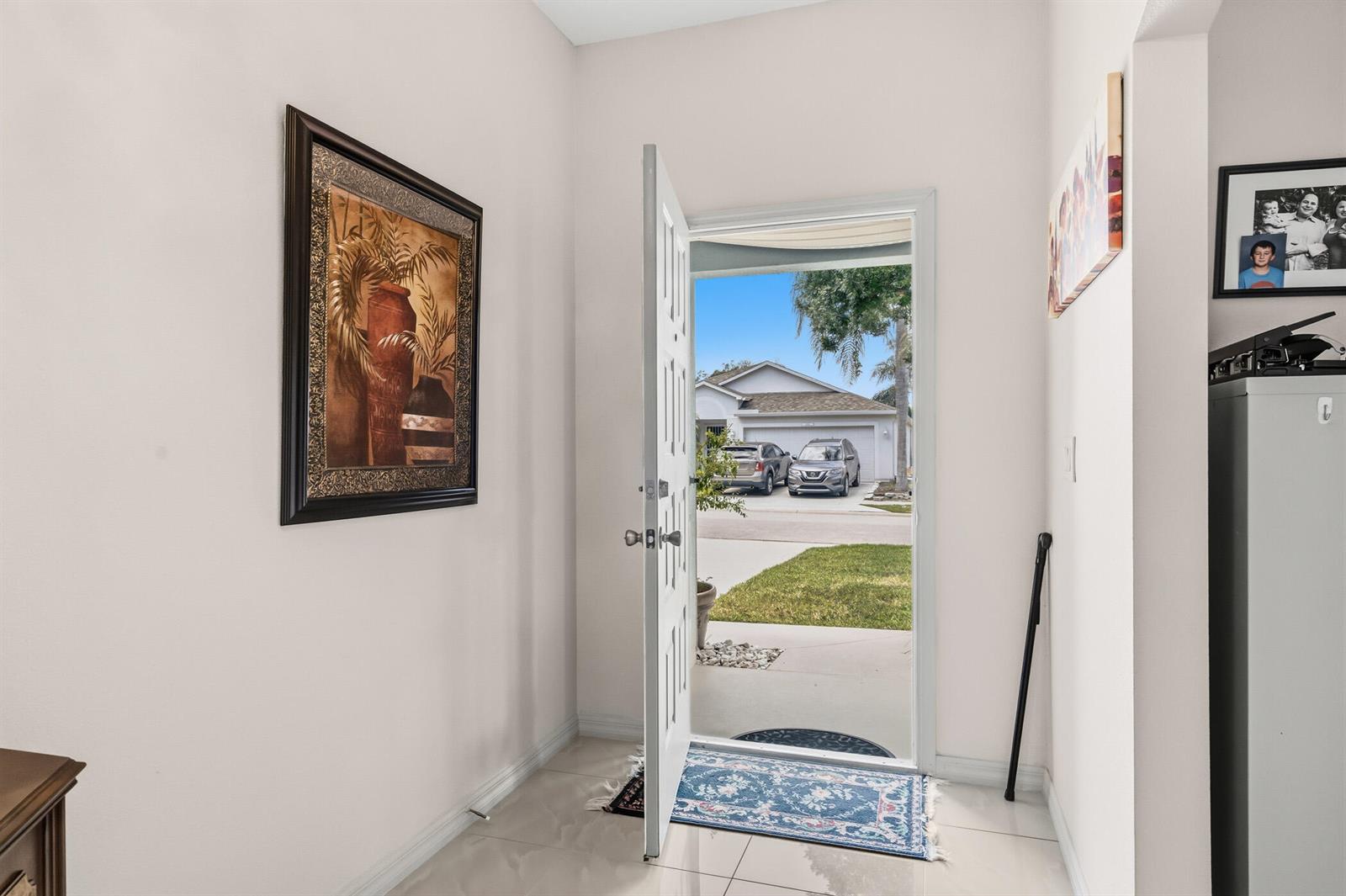 An open front door reveals a view of a suburban street and driveway from an entryway — 1013 E 13th Square, Vero Beach FL 32960, VERO BEACH, FL