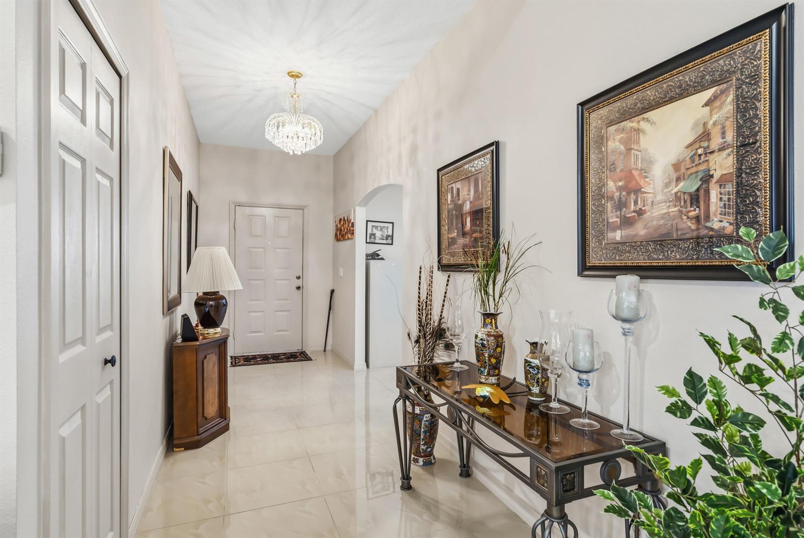 A bright entryway features a crystal chandelier, tiled floors, and a console table with decor — 1013 E 13th Square, Vero Beach FL 32960, VERO BEACH, FL