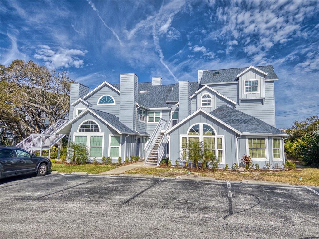 A multi-story blue-sided residential building with multiple gables and exterior staircases sits behind a parking lot — 4214 SUN VILLAGE COURT UNIT 380, NEW SMYRNA BEACH, FL