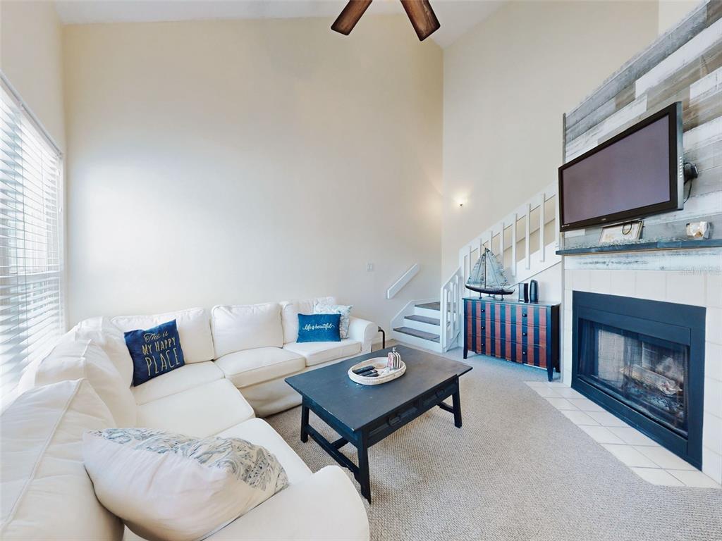 A living room features a white sectional sofa, a fireplace with a television, and stairs — 4214 SUN VILLAGE COURT UNIT 380, NEW SMYRNA BEACH, FL