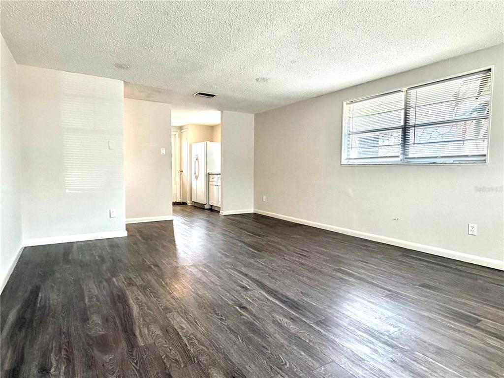 A living room with gray wood-look flooring, light walls, and a view into the kitchen — 5305 OAKWOOD COURT UNIT 17, TAMPA, FL