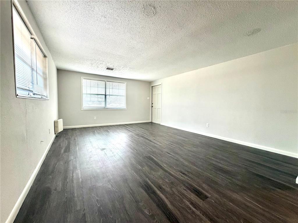 An empty room features dark wood-look flooring, light gray walls, and two windows — 5305 OAKWOOD COURT UNIT 17, TAMPA, FL