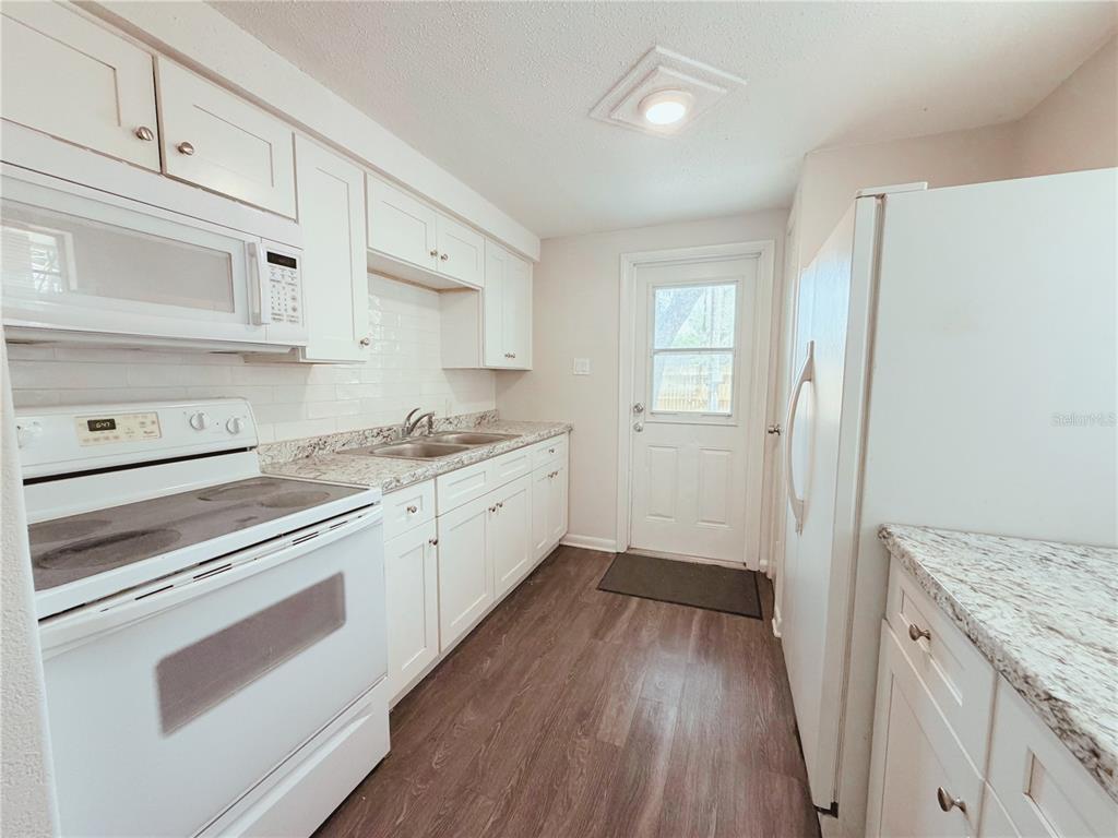 A kitchen features white cabinets, granite countertops, stainless steel appliances, and wood-look flooring — 5305 OAKWOOD COURT UNIT 17, TAMPA, FL