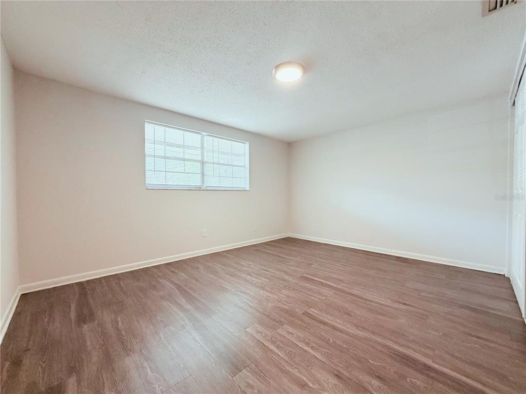An empty bedroom features light-colored walls, a single window with blinds, and wood-look flooring — 5305 OAKWOOD COURT UNIT 17, TAMPA, FL