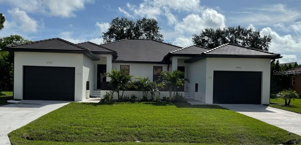 A modern single-story house with two garages, white stucco walls, and a dark tiled roof — 2926 MAGDALINA DRIVE, PUNTA GORDA, FL