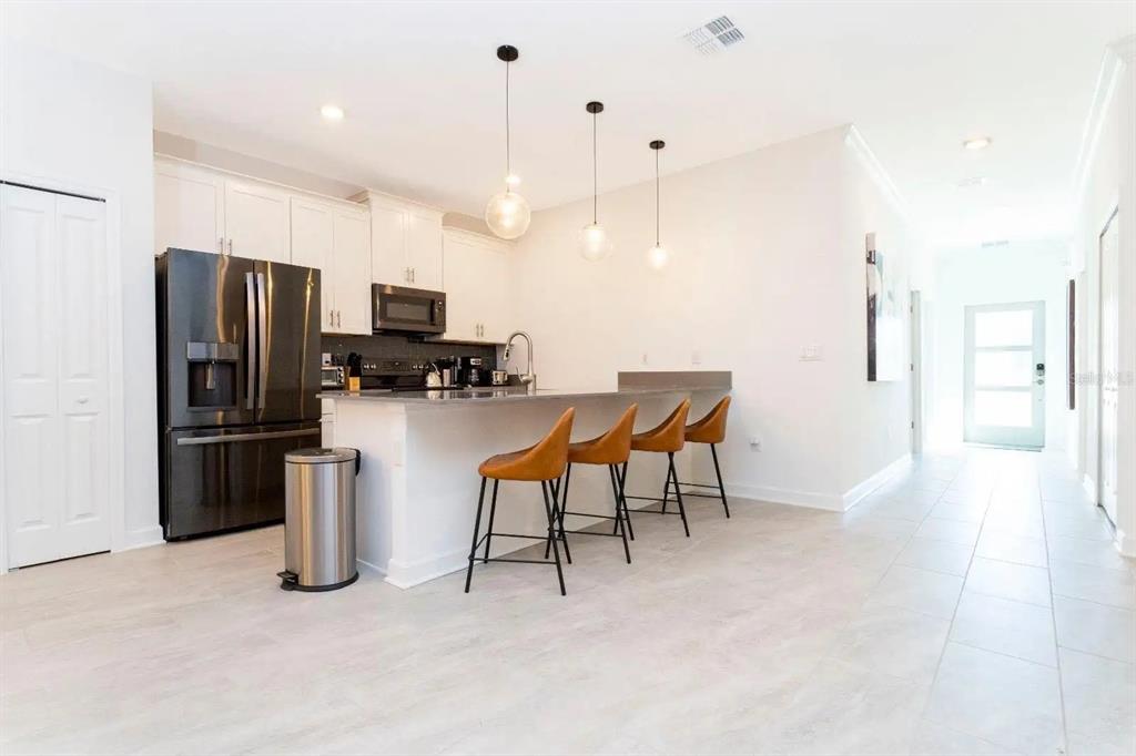 A modern kitchen features white cabinets, stainless steel appliances, and a breakfast bar with stools — 2994 PROTAGONIST STREET, KISSIMMEE, FL