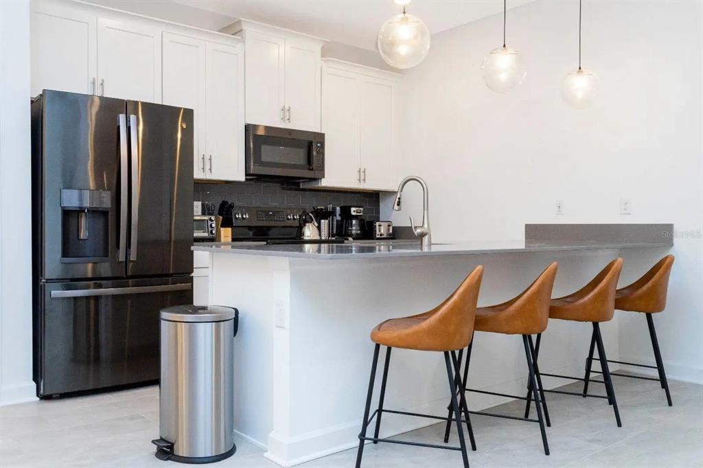 A modern kitchen features white cabinets, a black refrigerator, gray countertops, and four bar stools — 2994 PROTAGONIST STREET, KISSIMMEE, FL