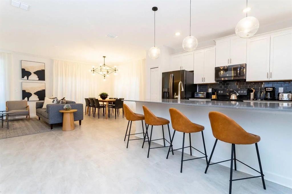 A modern open-concept kitchen with white cabinets, a gray island, and tan bar stools — 2994 PROTAGONIST STREET, KISSIMMEE, FL