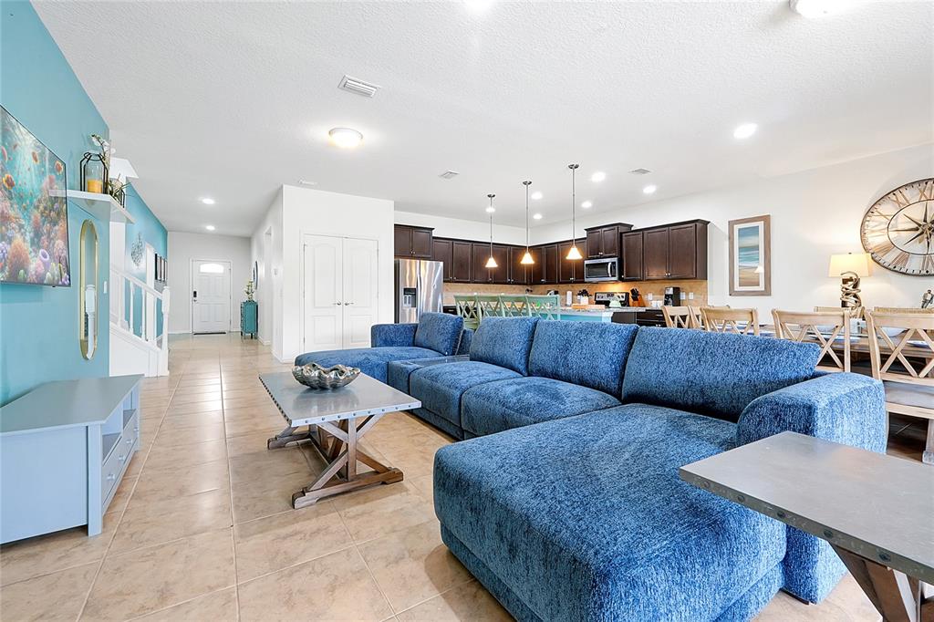 An open-concept living room features a blue sectional sofa, tile flooring, and a kitchen area — 1678 LIMA AVE, KISSIMMEE, FL