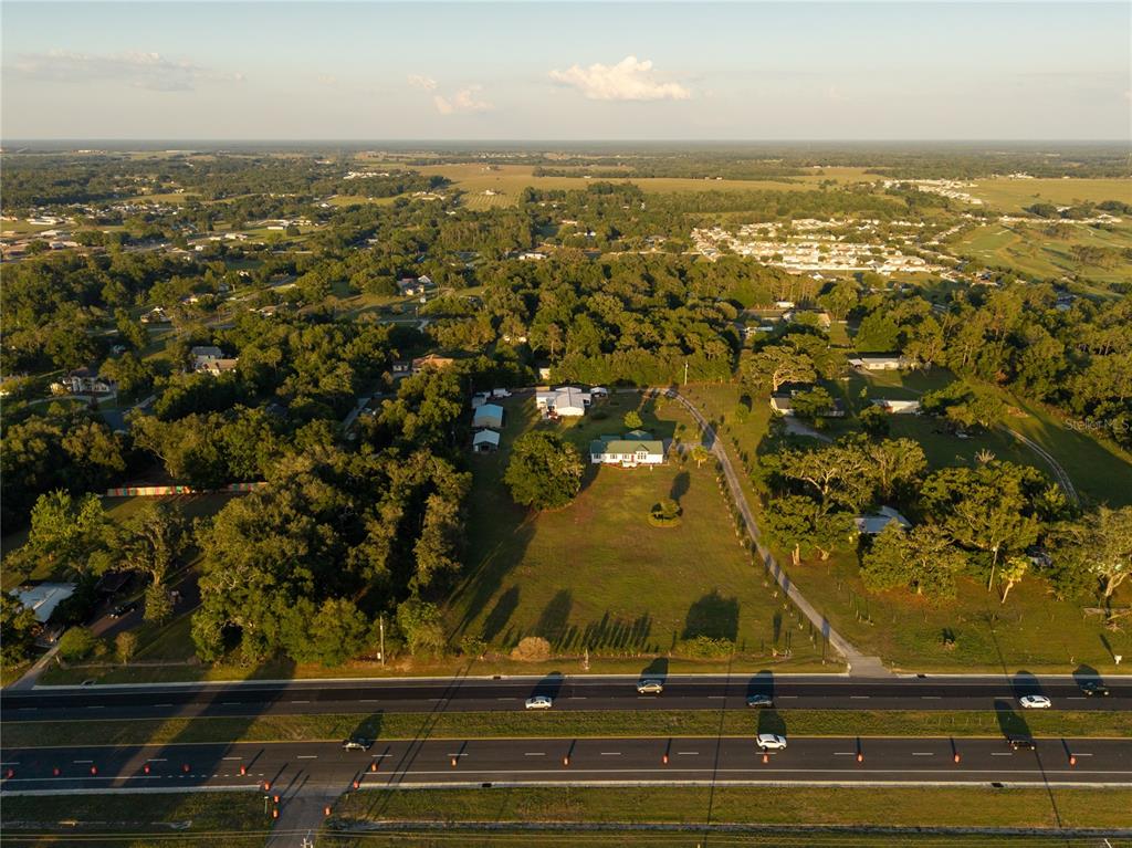 An aerial view shows a house and outbuildings on a large, grassy lot near a highway — 9712 US HIGHWAY 301, DADE CITY, FL