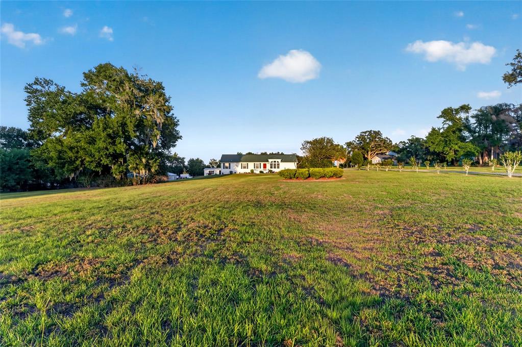 A white house with a green roof sits in the distance behind a large grassy field — 9712 US HIGHWAY 301, DADE CITY, FL