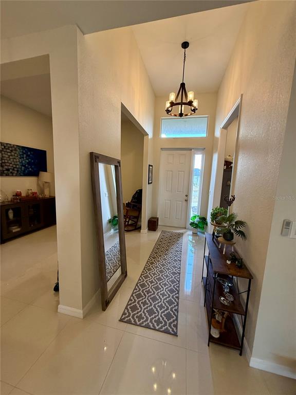 A bright entryway features a patterned runner rug, a tall floor mirror, and a chandelier — 3312 16TH STREET W, LEHIGH ACRES, FL