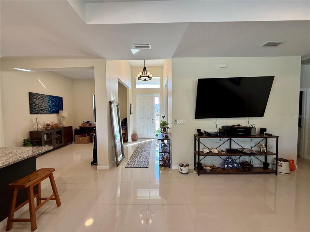 A bright living area features tile flooring, a mounted television, and an entryway with a chandelier — 3312 16TH STREET W, LEHIGH ACRES, FL