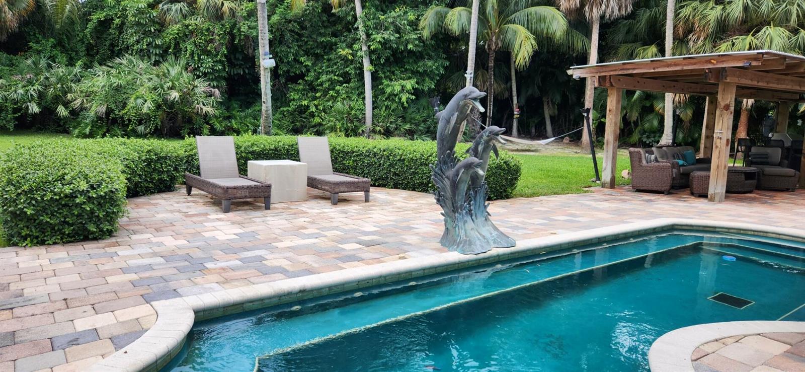 A backyard patio features a swimming pool, a dolphin sculpture, lounge chairs, and a gazebo — 1066 SE Saint Lucie Boulevard, Stuart FL 34996, STUART, FL
