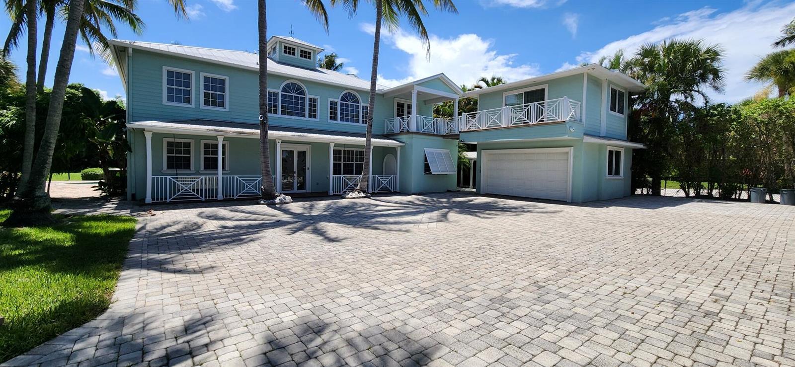A light blue two-story house with a paved driveway and palm trees under a blue sky — 1066 SE Saint Lucie Boulevard, Stuart FL 34996, STUART, FL